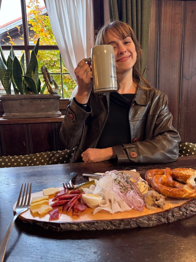 Woman holding a beer with a German food spread at a restaurant near Fussen, Germany